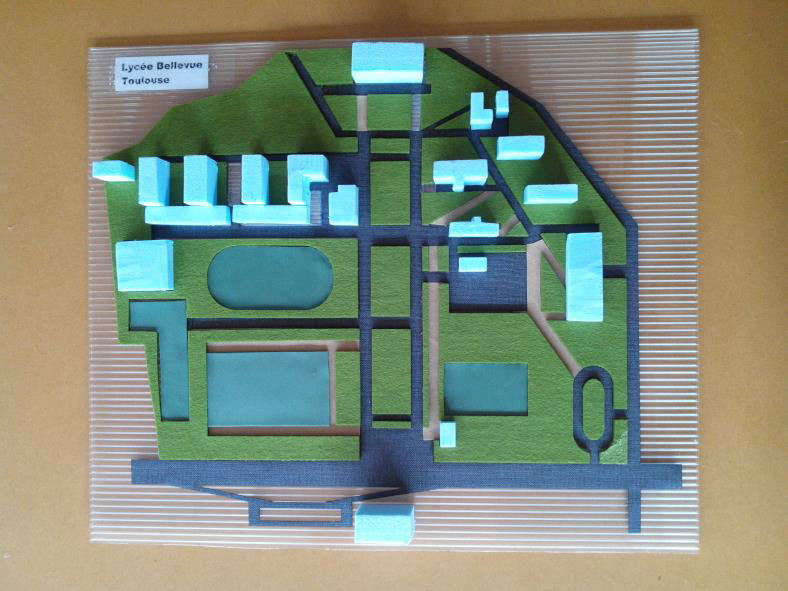 Photo du plan d'un lycée aux bâtiments très dispersés. Les espaces verts et les voies de circulations sont représentés en feutrine verte et en papier rugueux noirs découpés au laser. Les bâtiments, représentés en polystyrène, sont découpés manuellement.